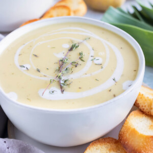 A large soup bowl full of potatoes and leeks blended into a soup being served with toasted baguette bread.