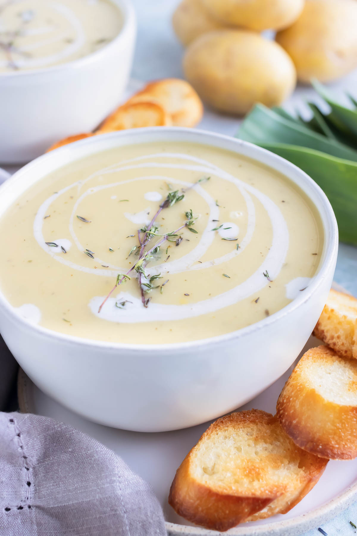 A large soup bowl full of potatoes and leeks blended into a soup being served with toasted baguette bread.