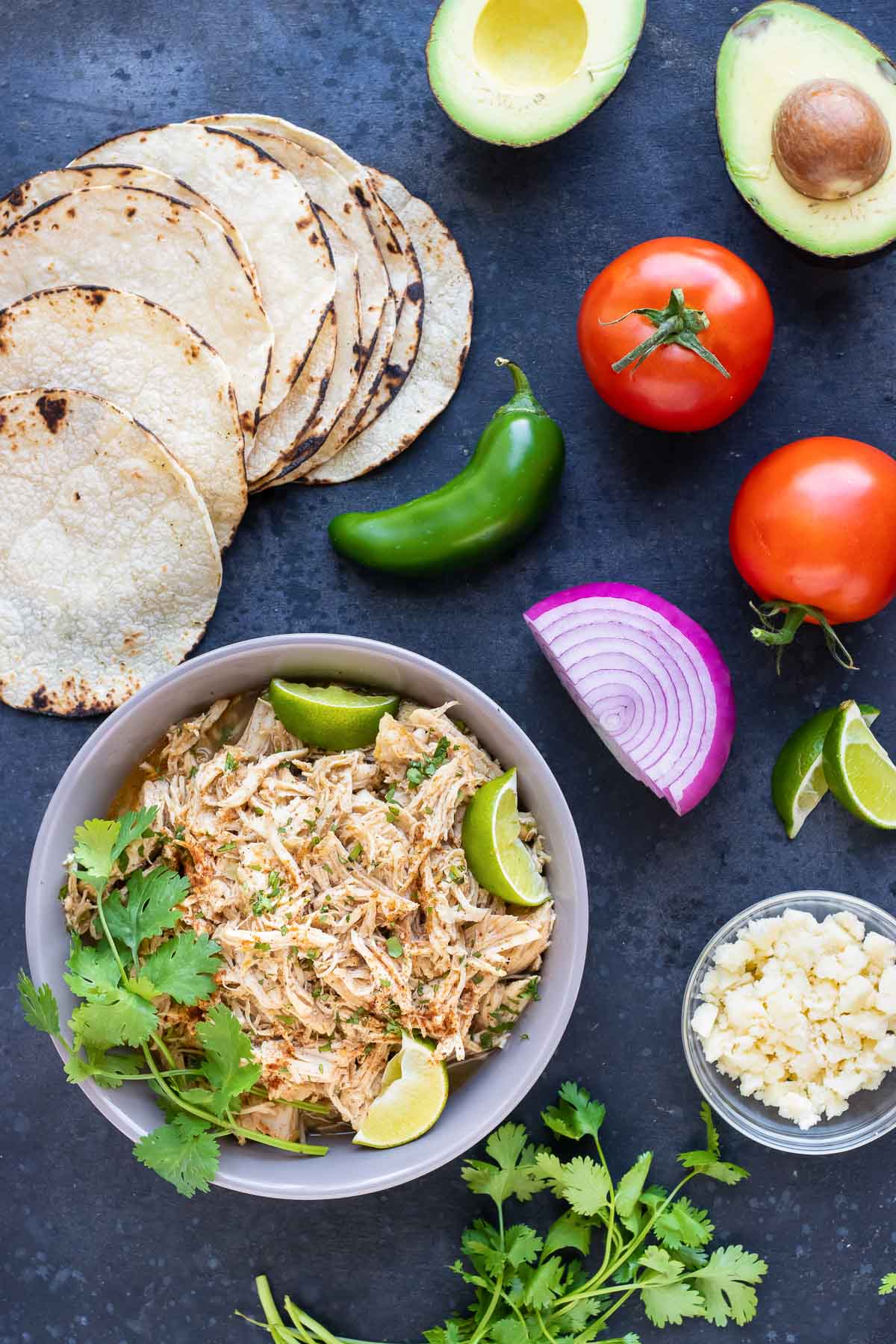 Tortillas, avocado, tomato, shredded chicken, and Cotija cheese as the ingredients for an easy chicken taco recipe.