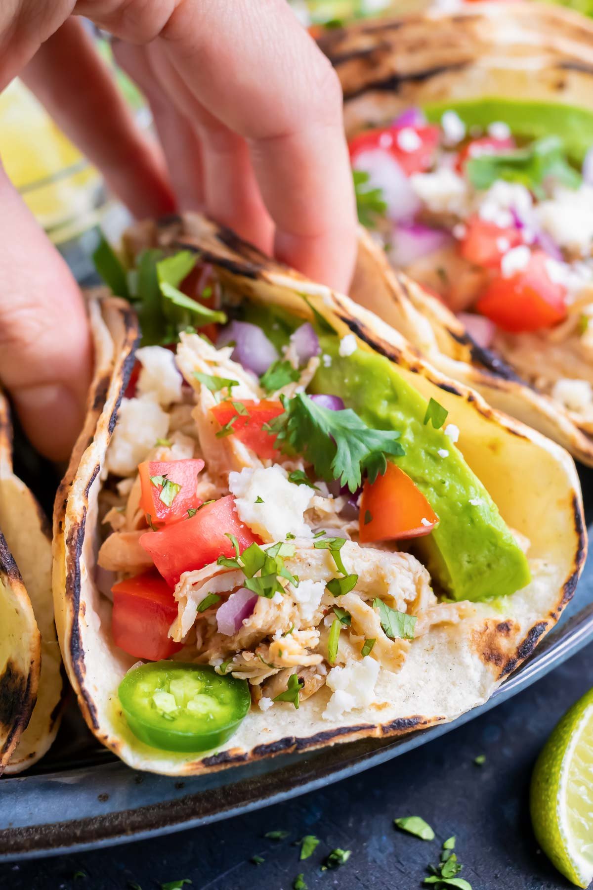 A hand picking up a corn tortilla full of Instant Pot salsa shredded chicken with tomatoes and avocado.