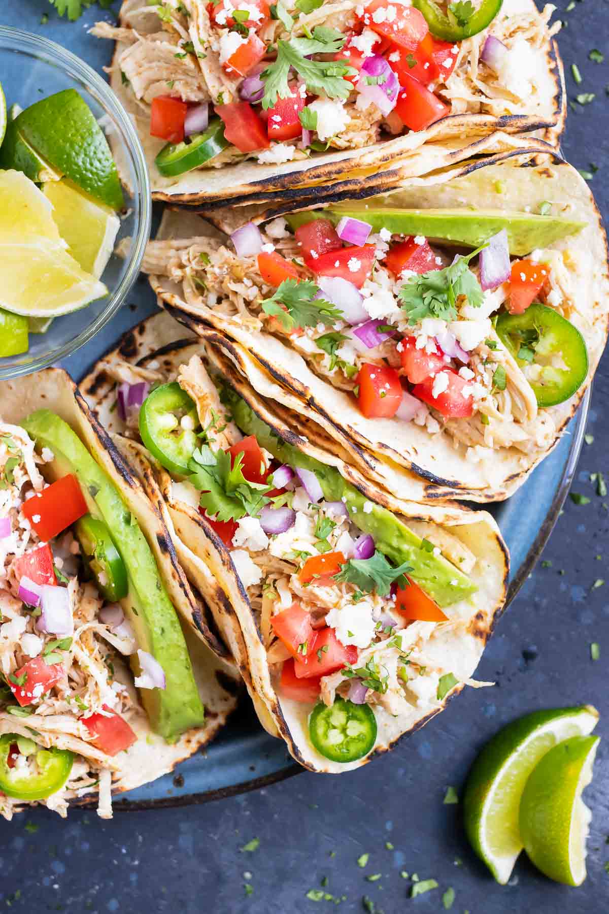 An easy taco recipe that is full of shredded salsa chicken with taco seasoning mix, tomatoes, avocado, and cheese.