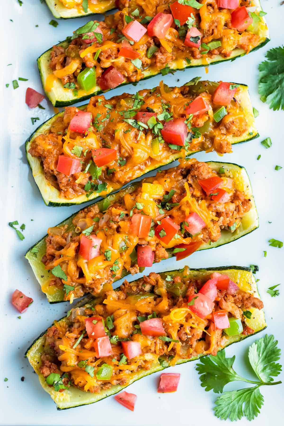 Four taco stuffed zucchini boats are on a platter filled with a ground meat and cheese.
