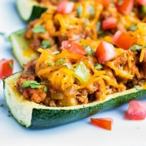 Mexican stuffed zucchini boats are filled with a ground taco meat and topped with cheese on a plate.