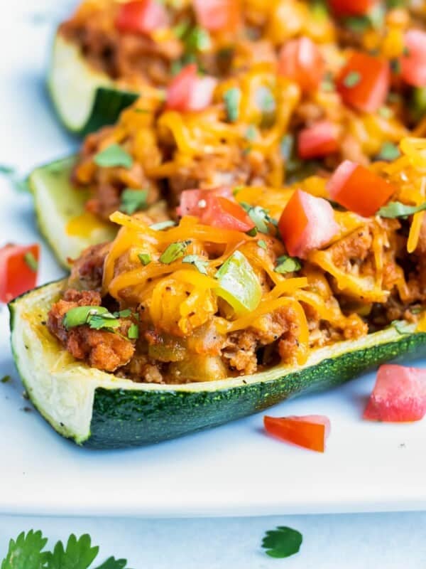 Mexican stuffed zucchini boats are filled with a ground taco meat and topped with cheese on a plate.