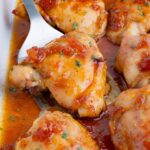 A spatula scoops a chicken thigh cooked in a sweet and savory sauce from a baking dish.