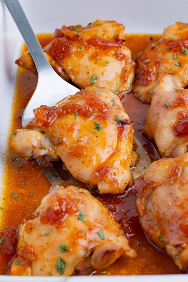 A spatula scoops a chicken thigh cooked in a sweet and savory sauce from a baking dish.