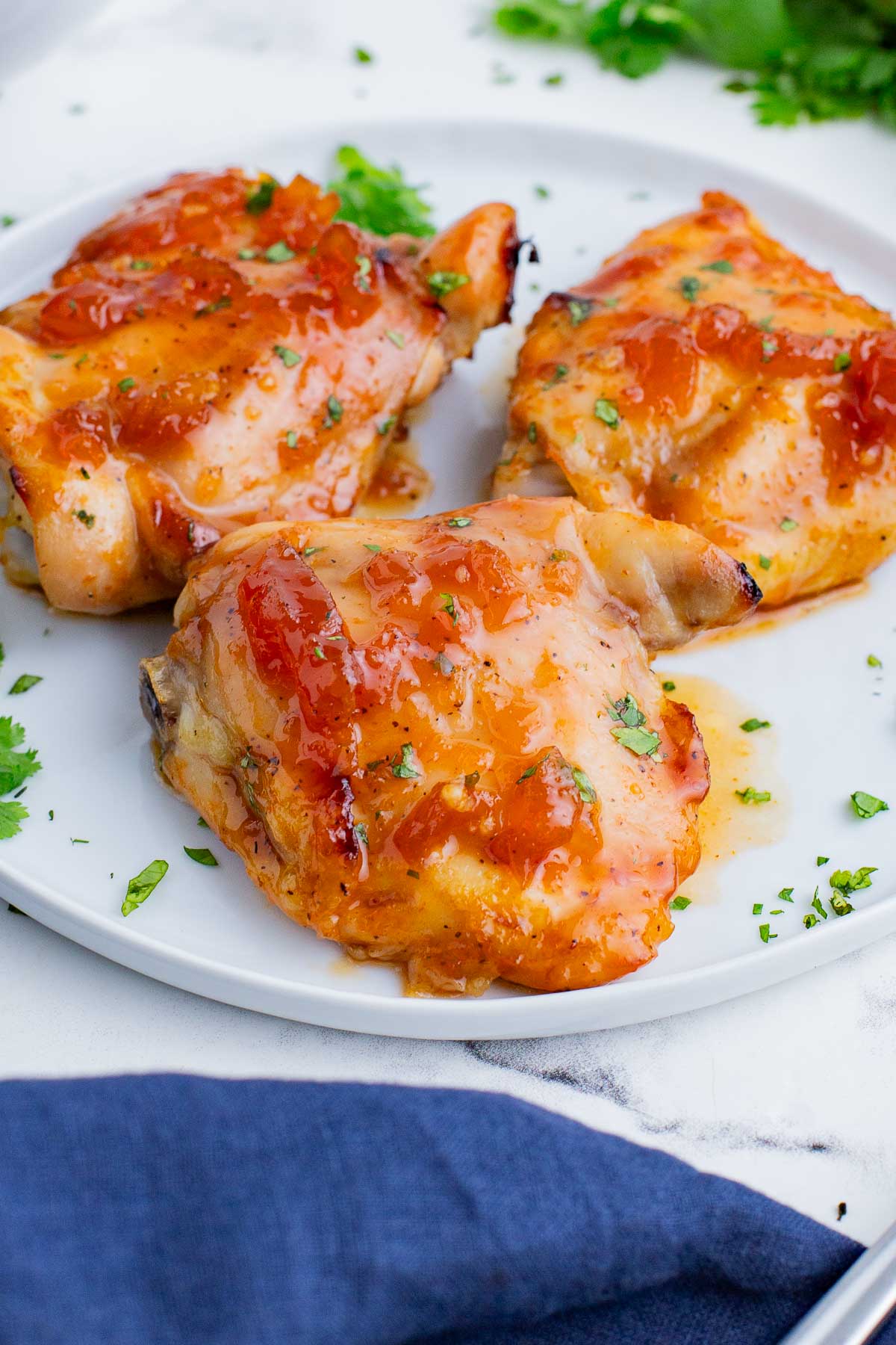 Three chicken thighs in an apricot sauce are served on a white plate.