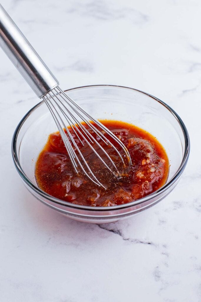 A whisk stirring together the sweet and spicy apricot bbq glaze in a glass bowl.