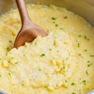 Cheesy gluten-free grits in a stainless steel pot with a wooden spoon.