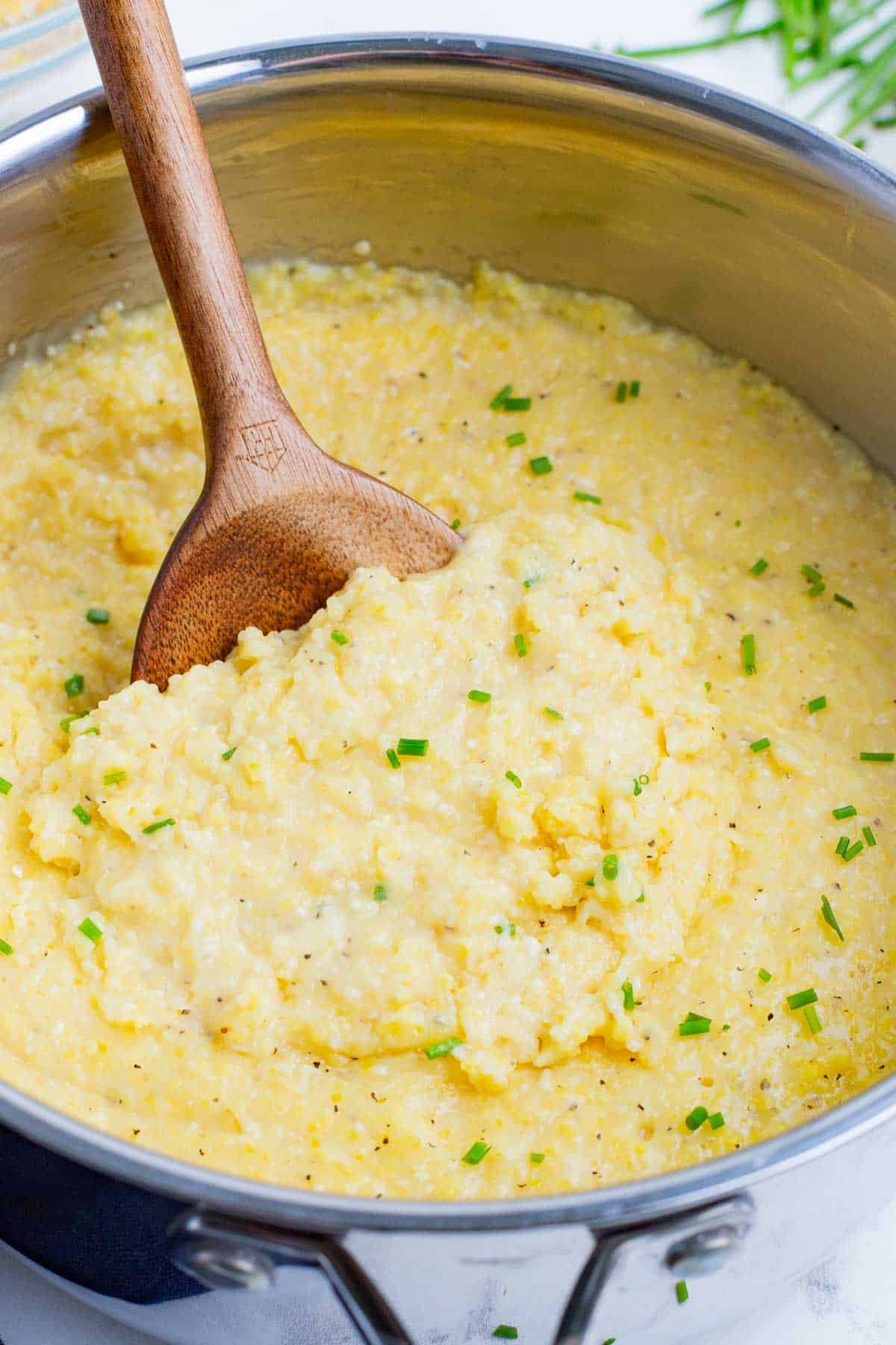 Cheesy gluten-free grits in a stainless steel pot with a wooden spoon.