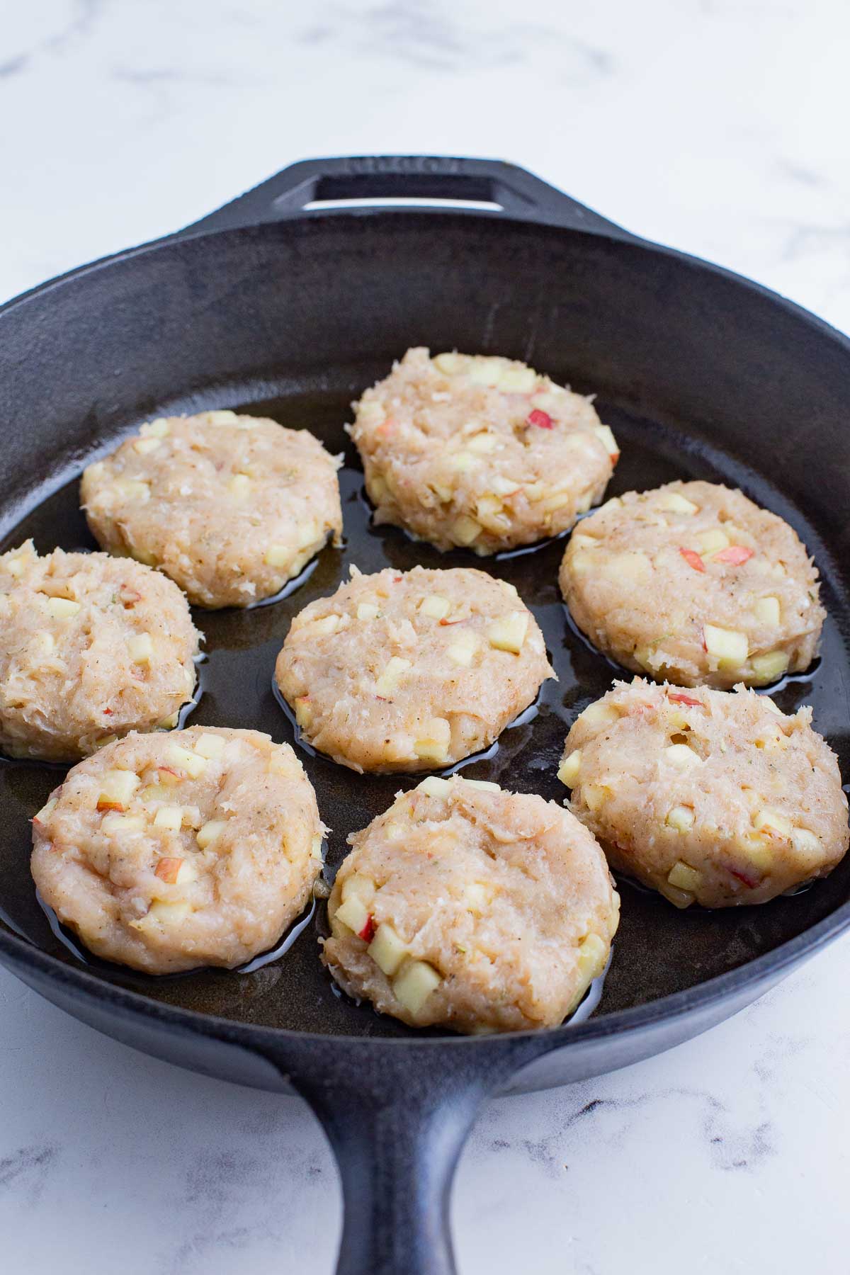 The sausage patties are cooked in a heated cast iron skillet.