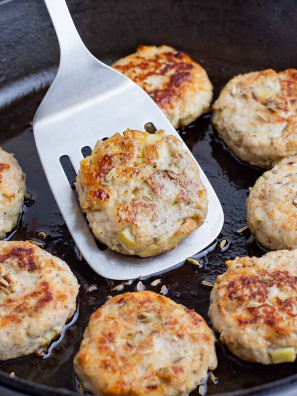 A spatula picks up a cooked apple sausage patty from the skillet.