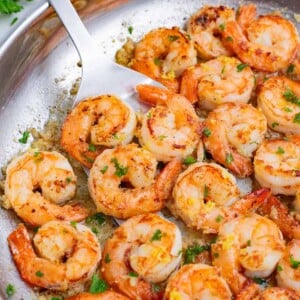 A spatula flips garlic butter shrimp in a skillet.