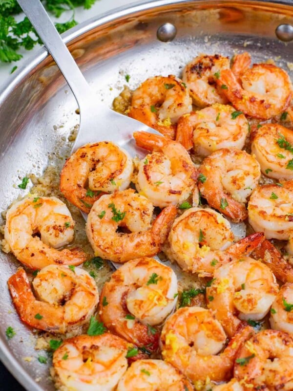 A spatula flips garlic butter shrimp in a skillet.