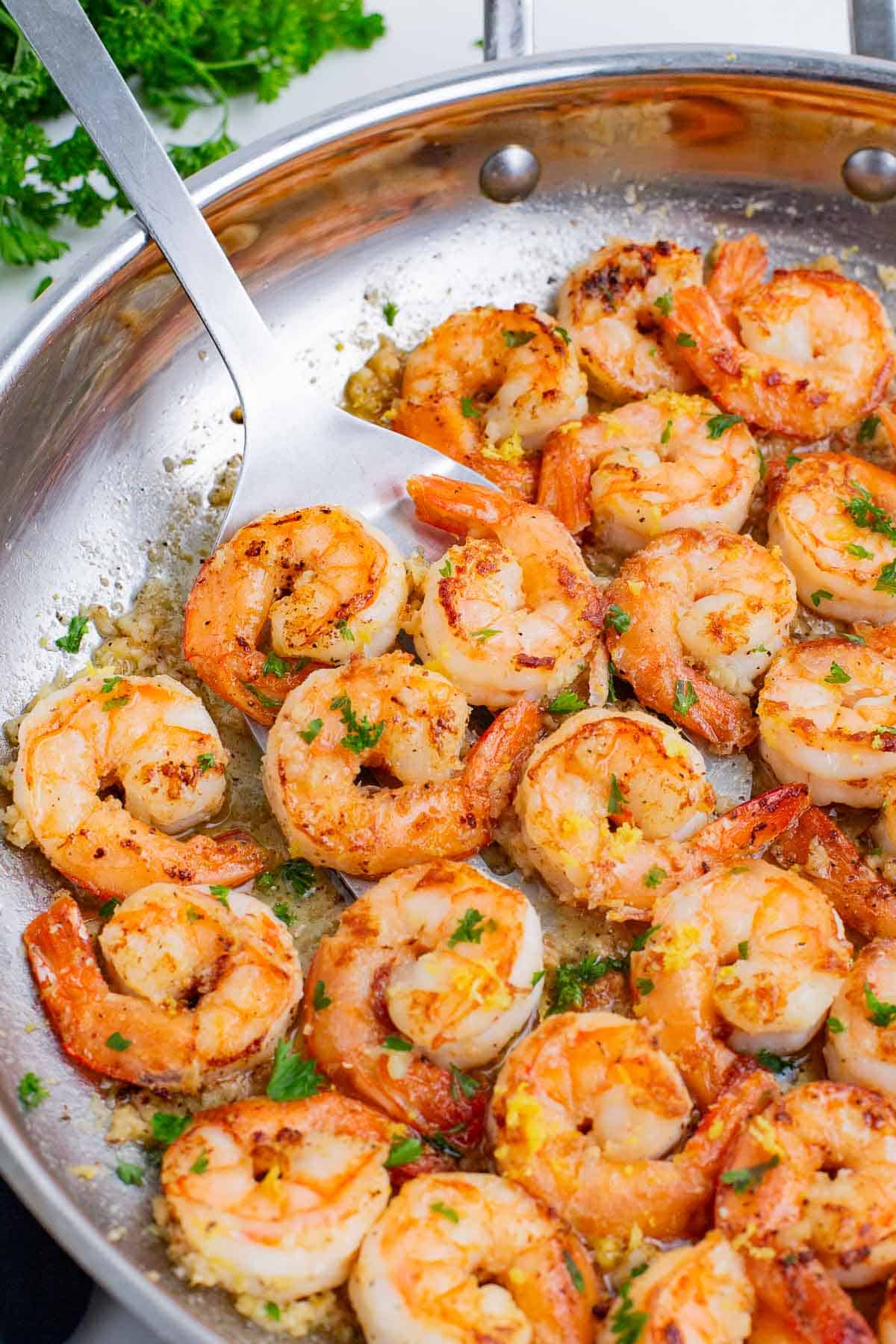 A spatula flips garlic butter shrimp in a skillet.