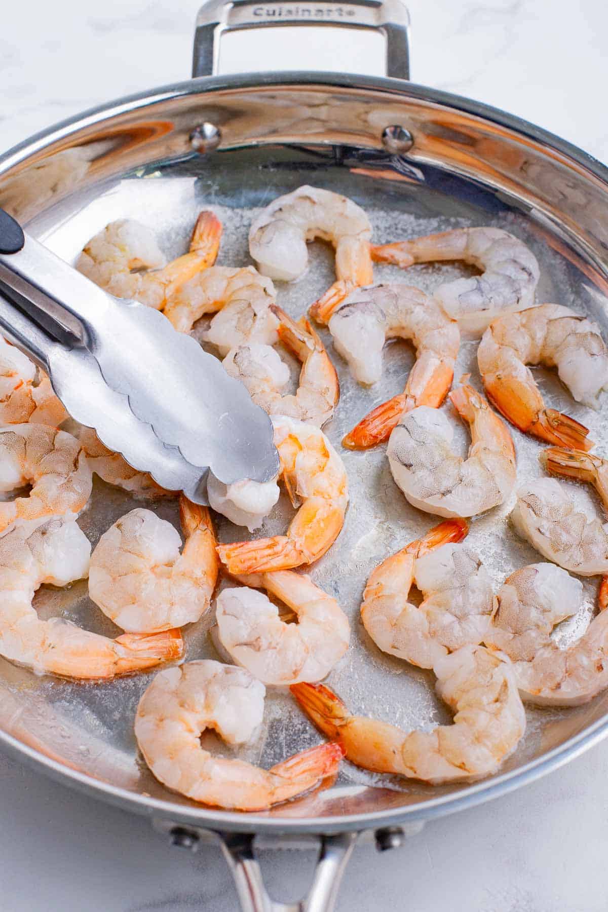 Tongs turn shrimp over as it cooks.