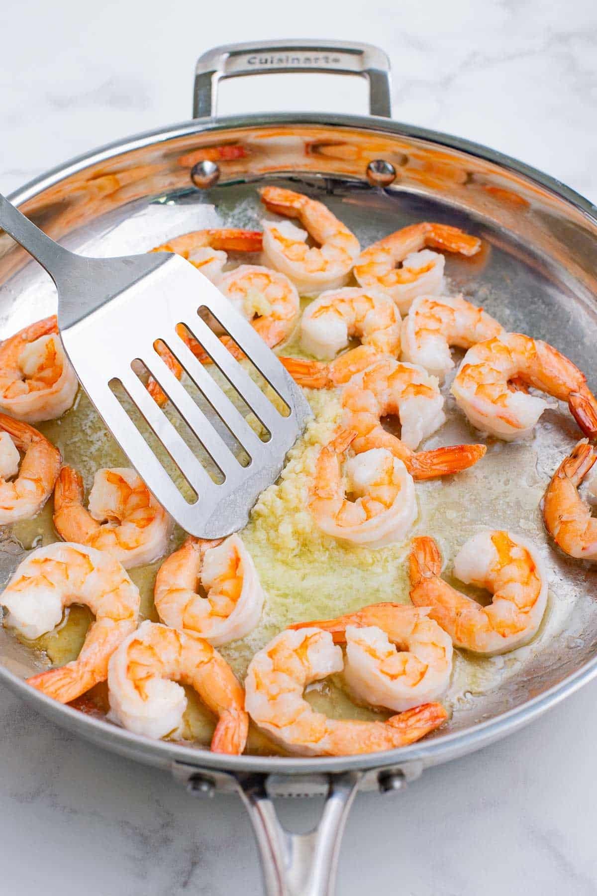 A spatula stirs garlic, butter, and shrimp.
