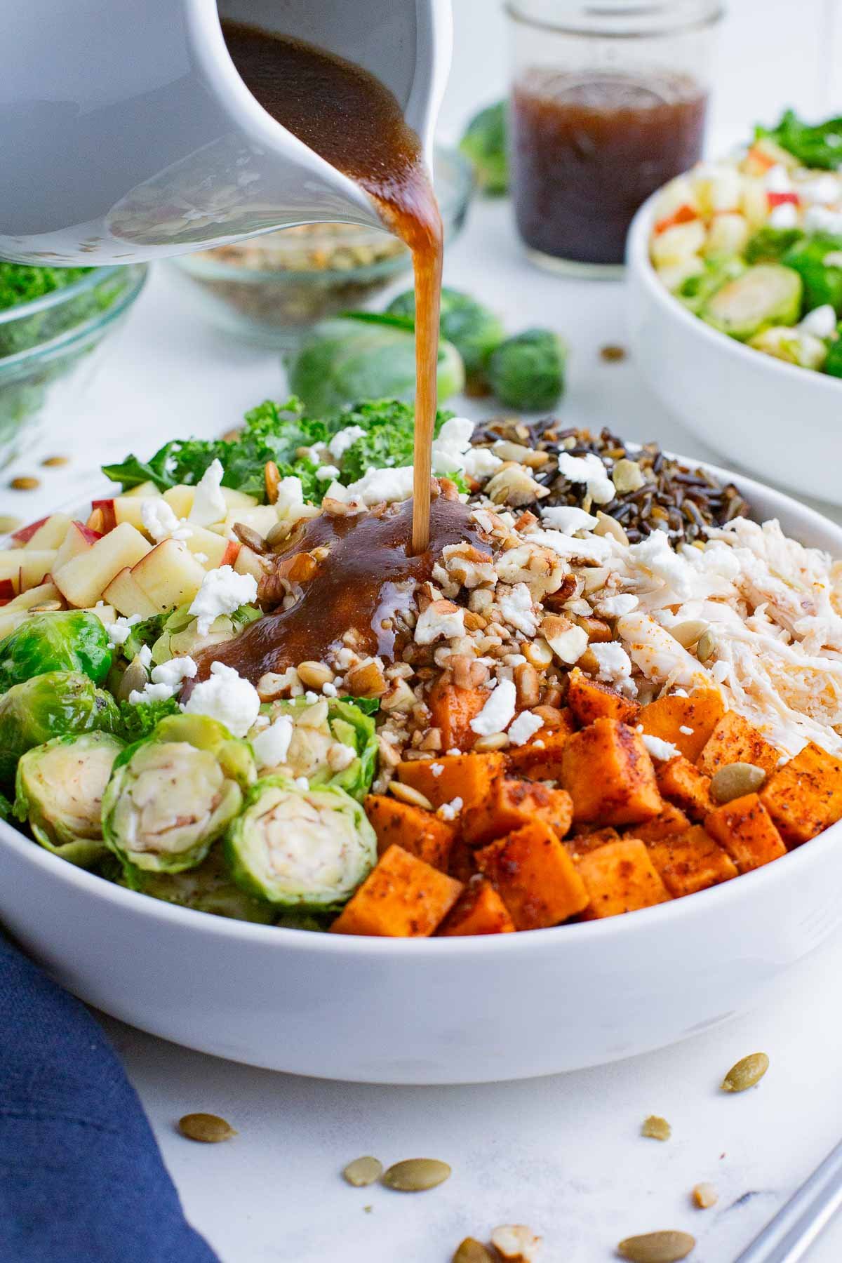 Balsamic dressing is poured over the ingredients of a harvest bowl.