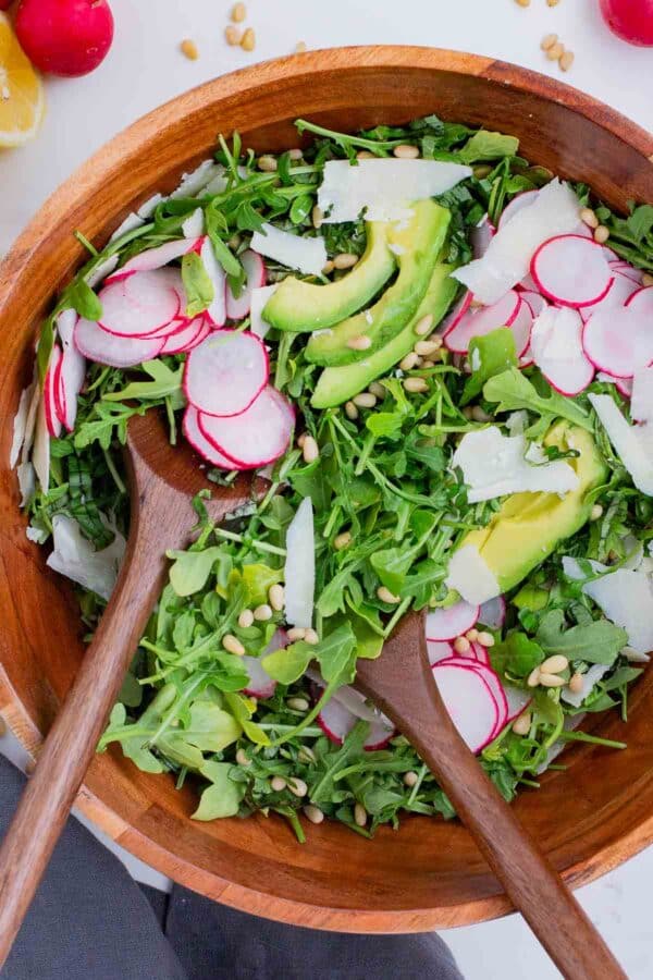 Salad tongs toss a lemon arugula salad together.