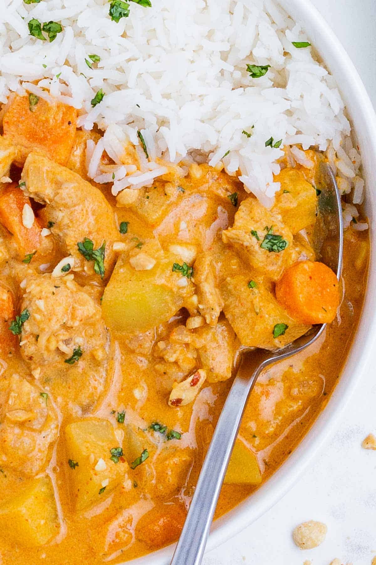 A spoon is used to serve Massaman curry and rice from a white bowl.