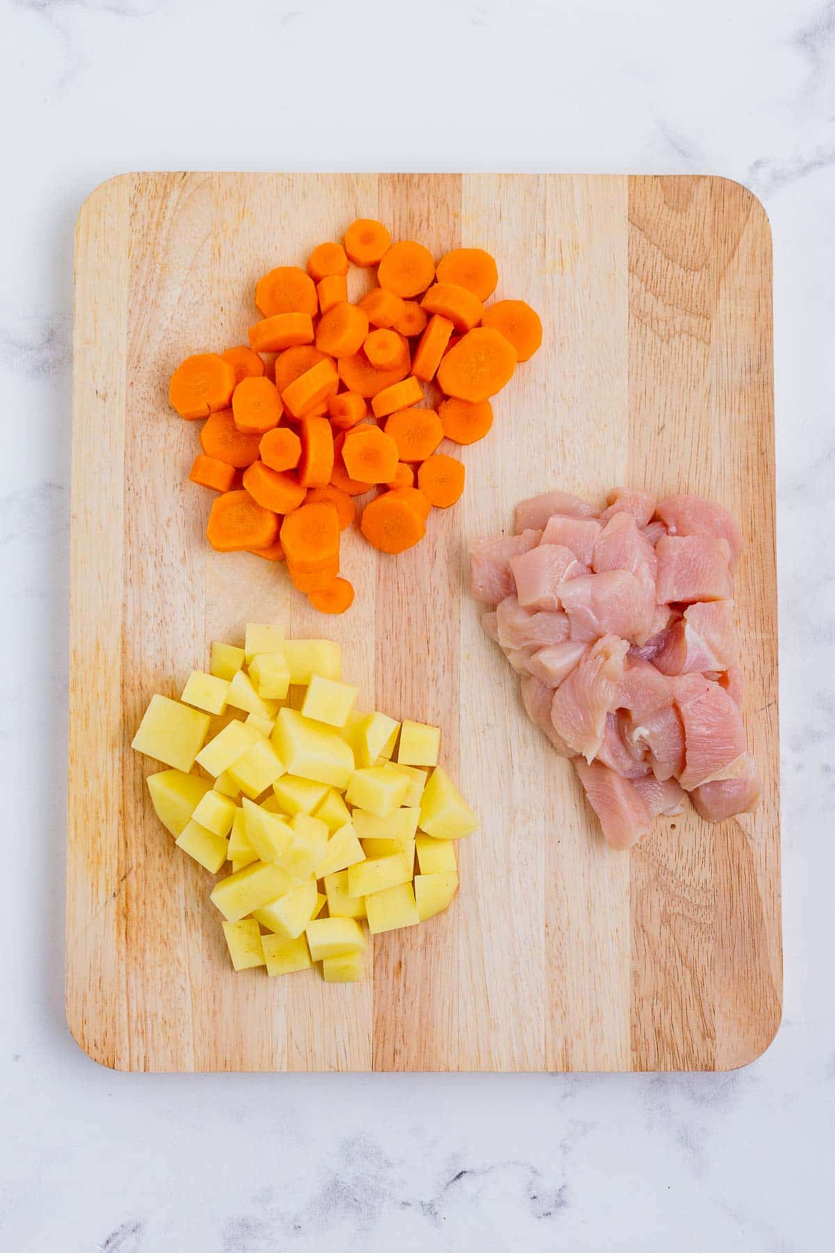 Carrots, potatoes, and chicken are cut into chunks.