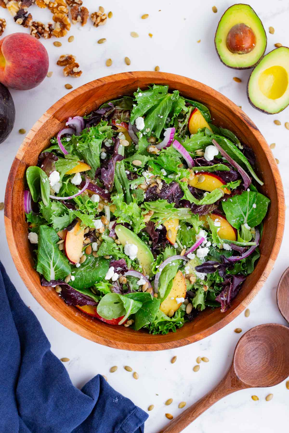 An overhead shot of a peach and greens salad in a wooden bowl.