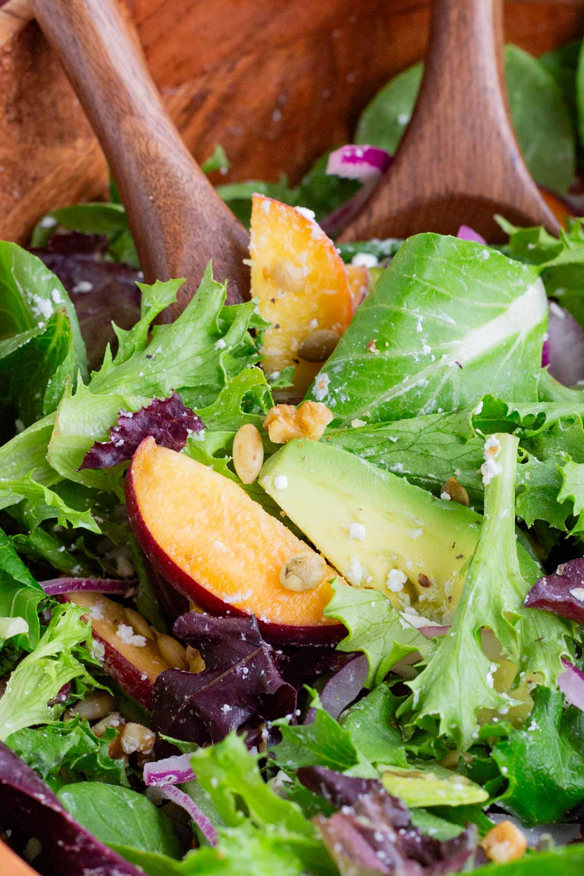 Wooden spoons stir a healthy peach salad.