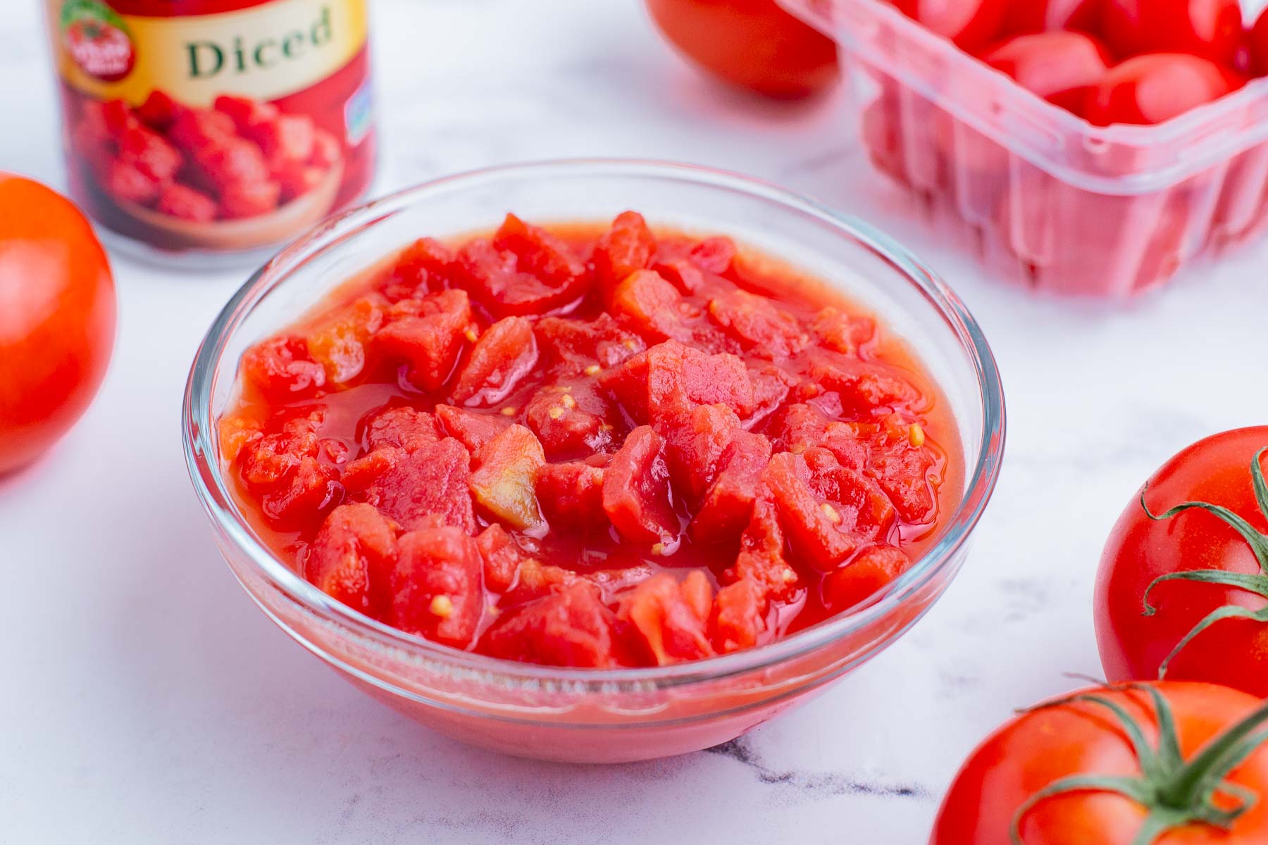 Canned diced tomatoes in a glass bowl with fresh tomatoes nearby.