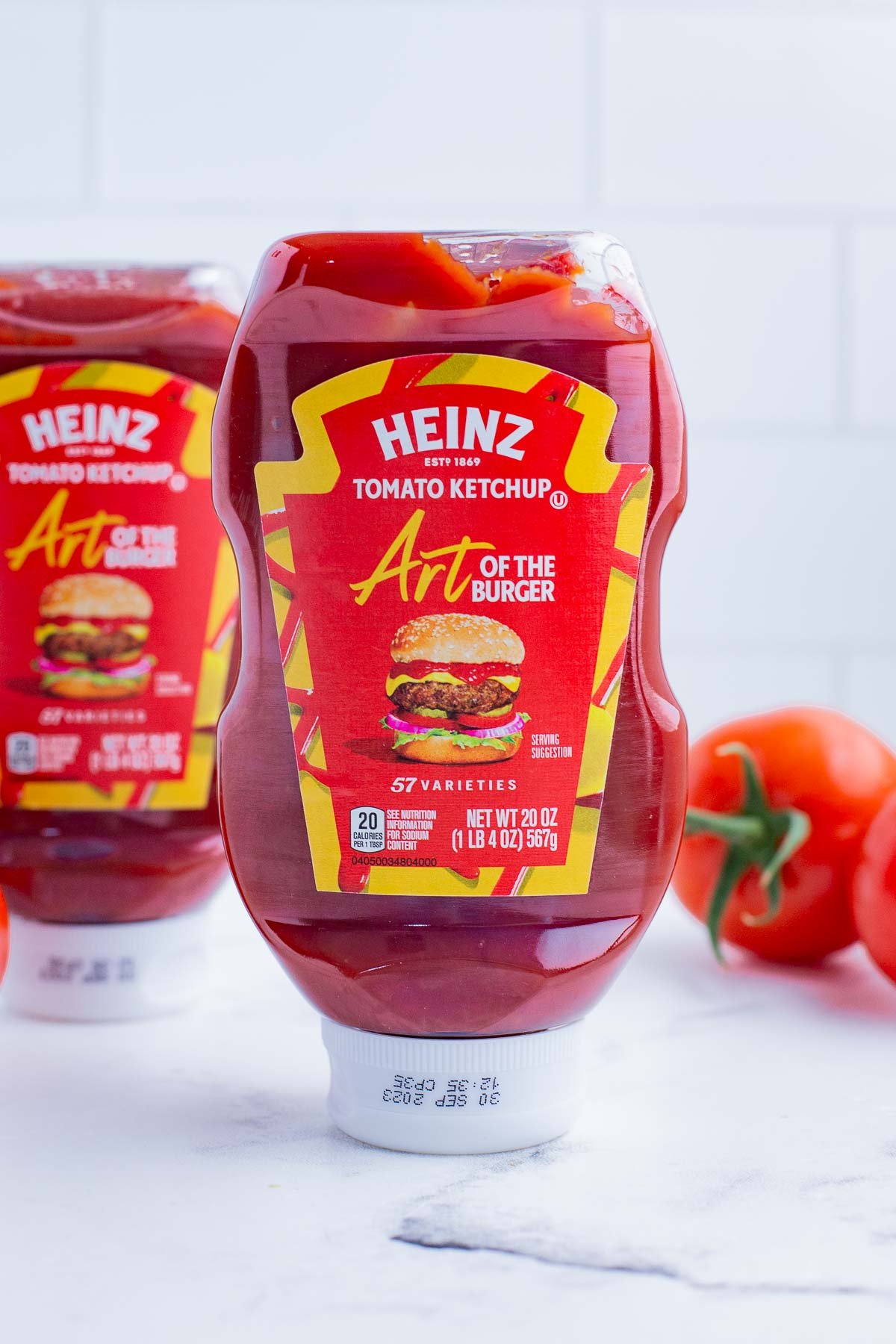 Ketchup bottles with fresh tomatoes in the background.