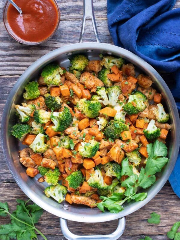 A large skillet full of honey BBQ chicken, sweet potatoes, and broccoli for a one-pot meal.