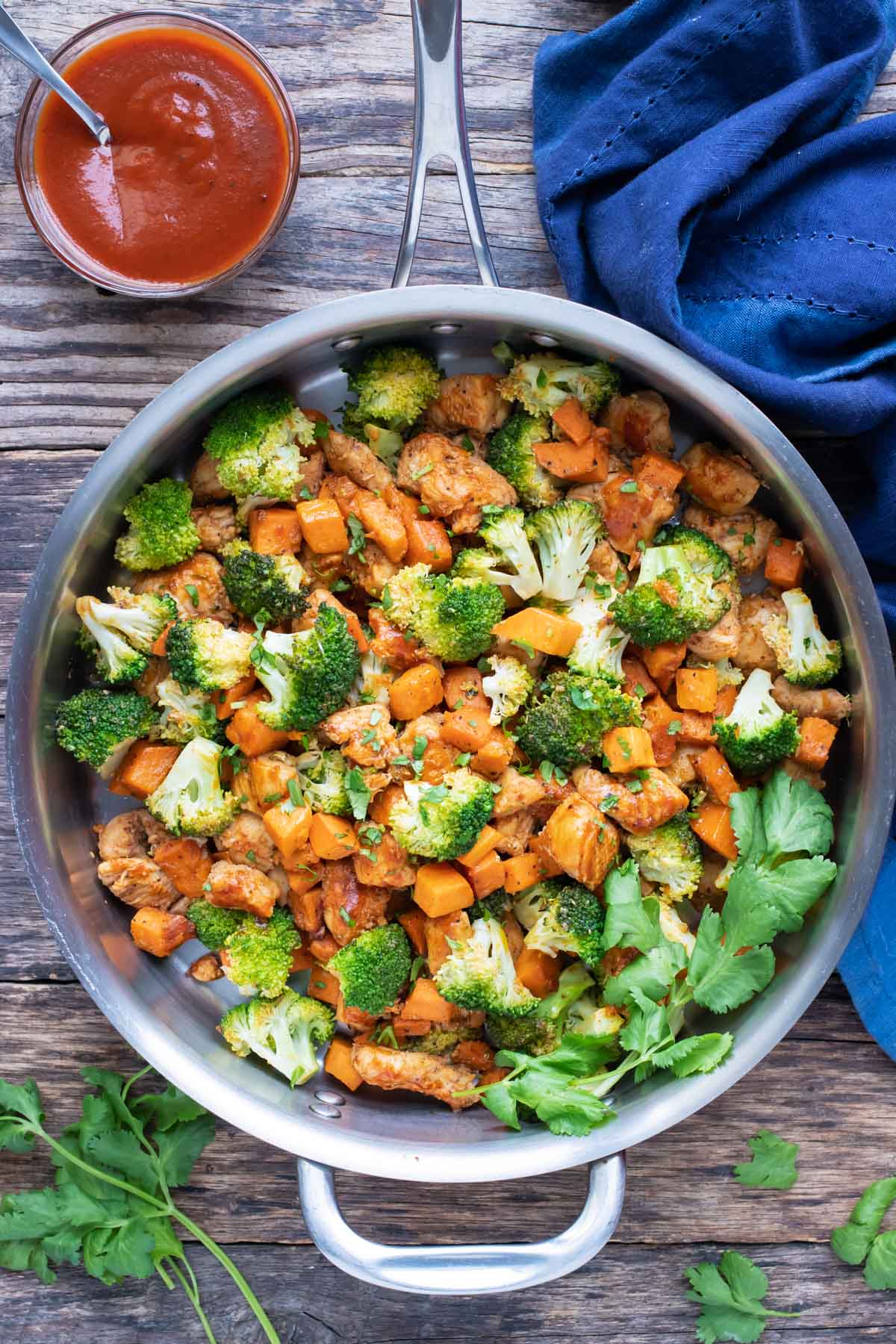 A large skillet full of honey BBQ chicken, sweet potatoes, and broccoli for a one-pot meal.