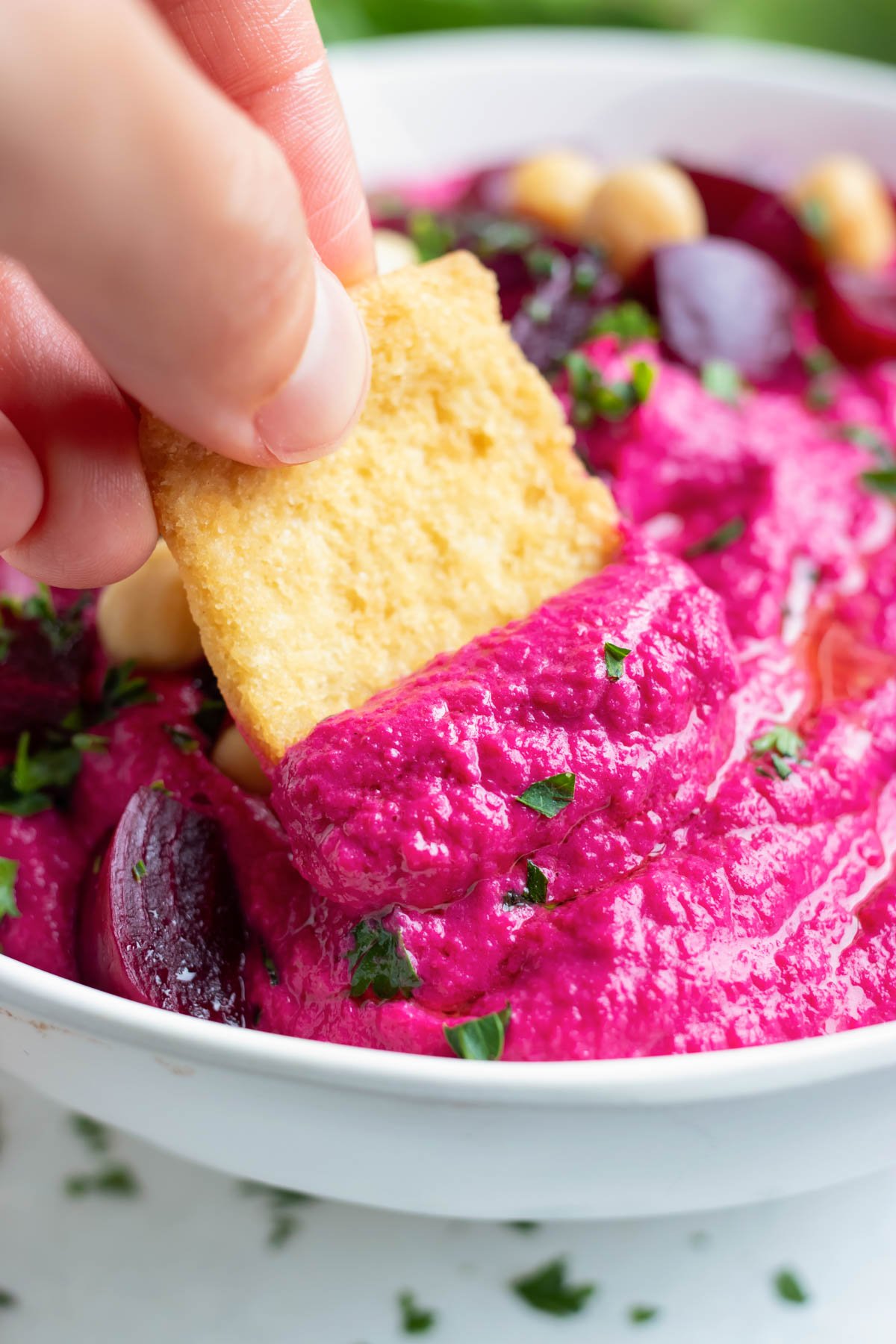 A gluten-free cracker is dipped into this creamy, homemade hummus.