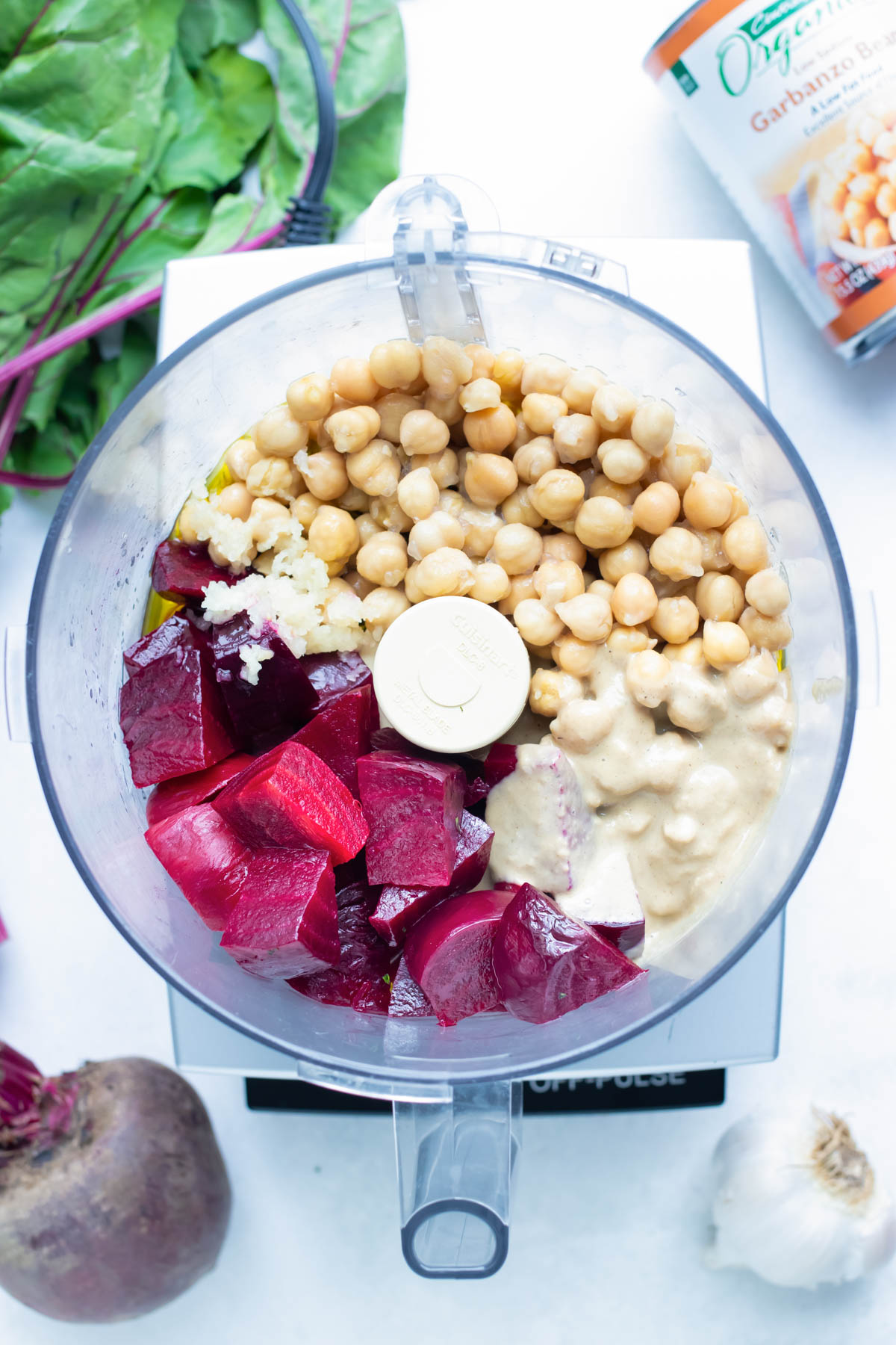 Chickpeas, roasted beets, tahini paste, garlic, and olive oil are added to a food processor.
