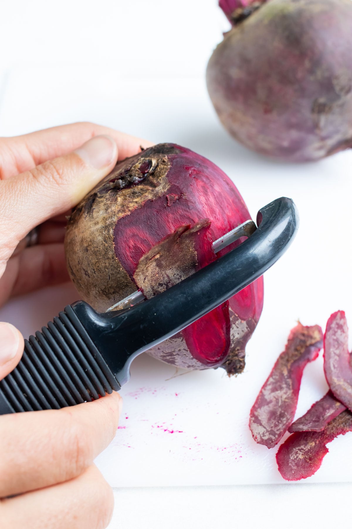 A fresh red beet being peeled with a vegetable peeler before making beet soup.
