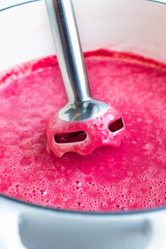 An immersion blender blending beet soup until smooth and creamy right in the pot.