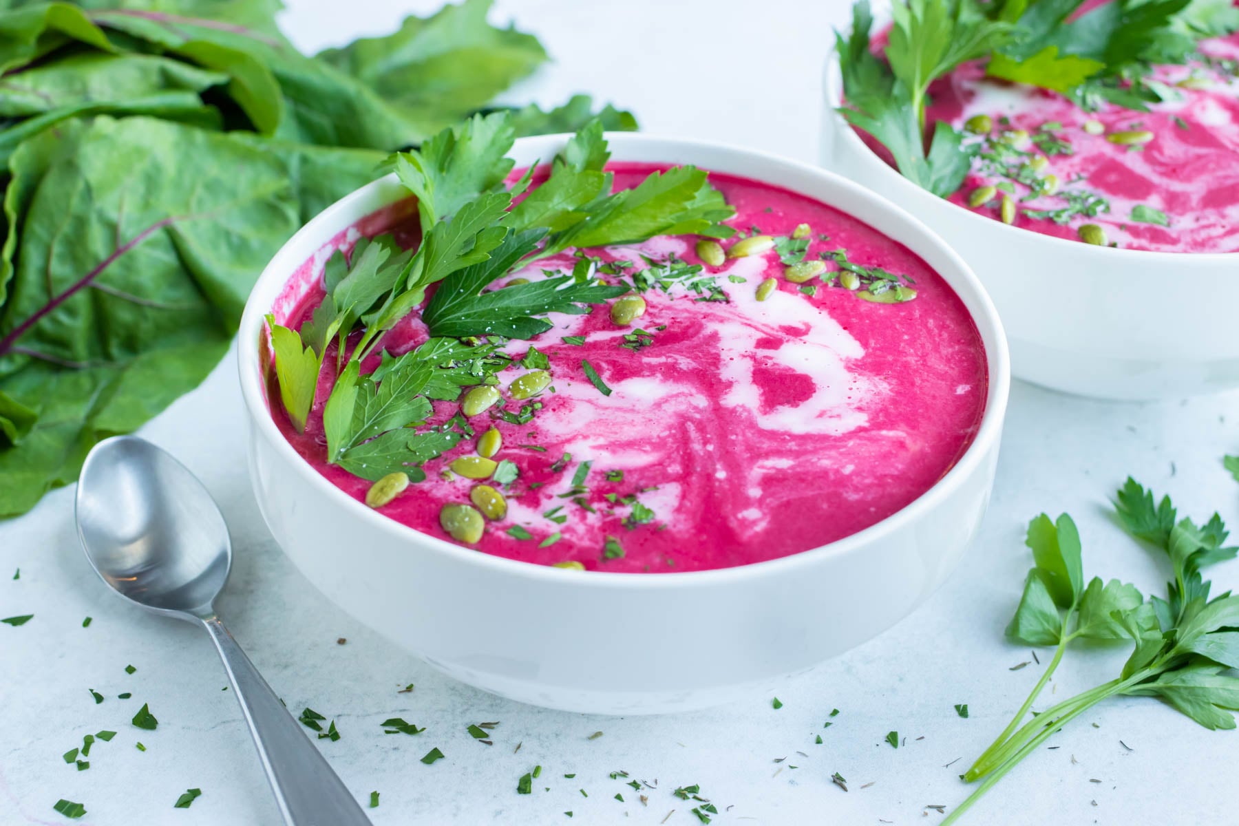 Vegan beet soup served in two white bowls with a spoon and fresh herbs.