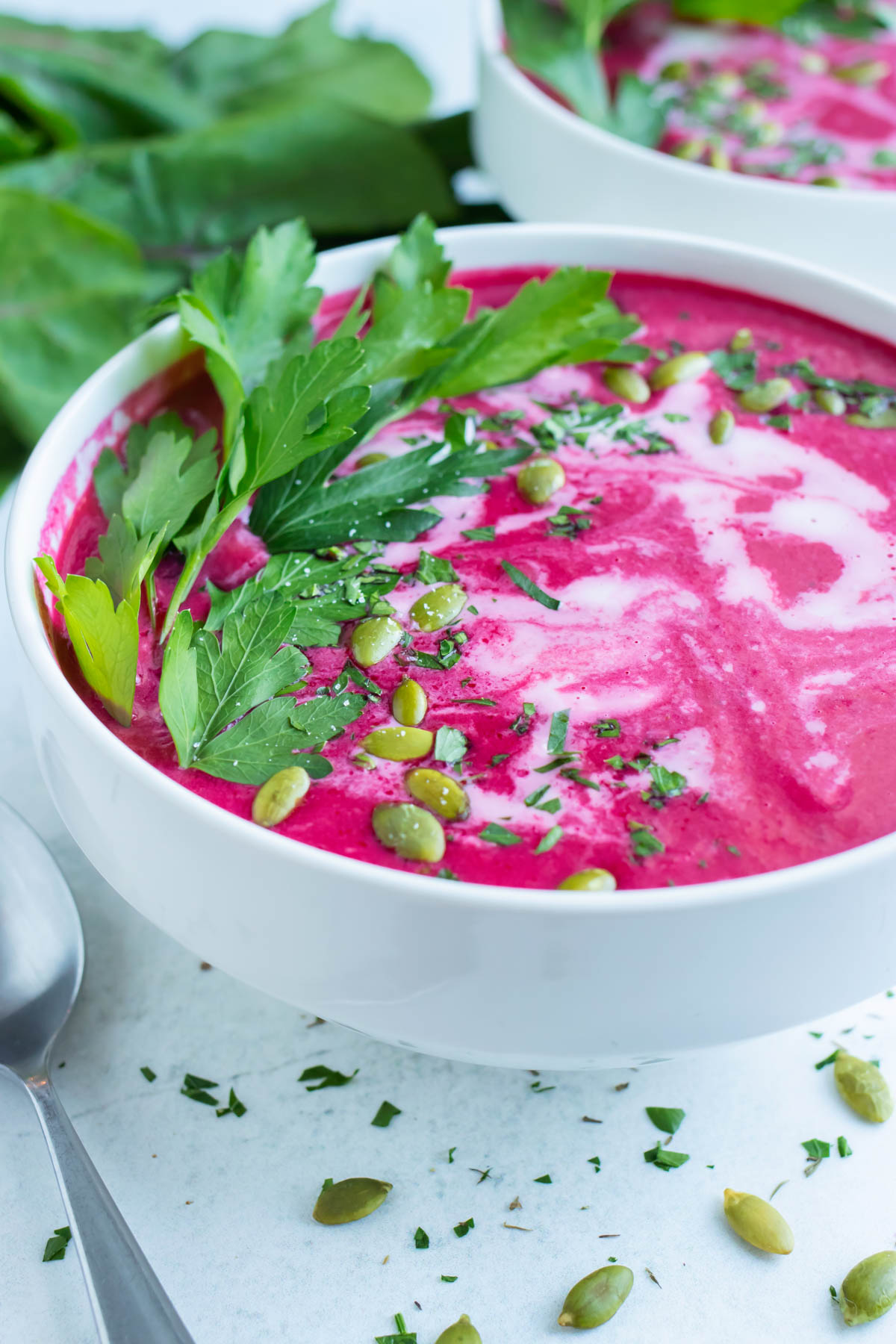 A white bowl full of a vegan and creamy beet soup recipe with cilantro and pumpkin seeds on top.