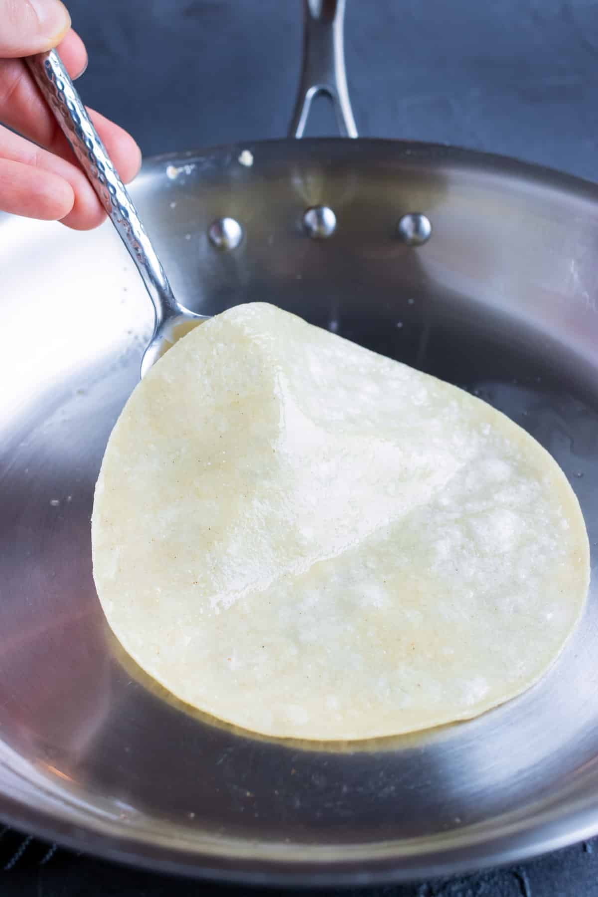 A corn tortilla being lightly toasted in coconut oil in a skillet for a taco.