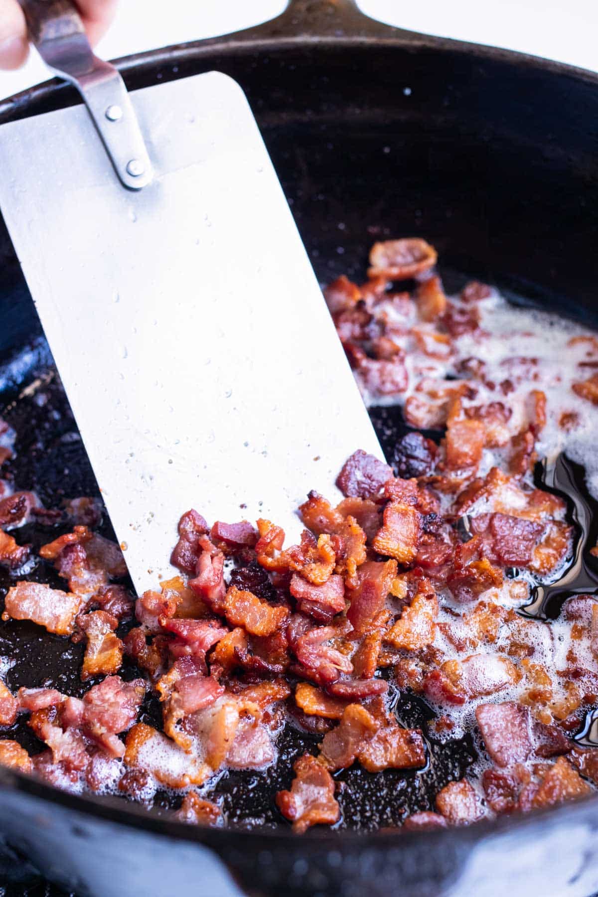 Bacon bits are cooked in a cast-iron skillet.