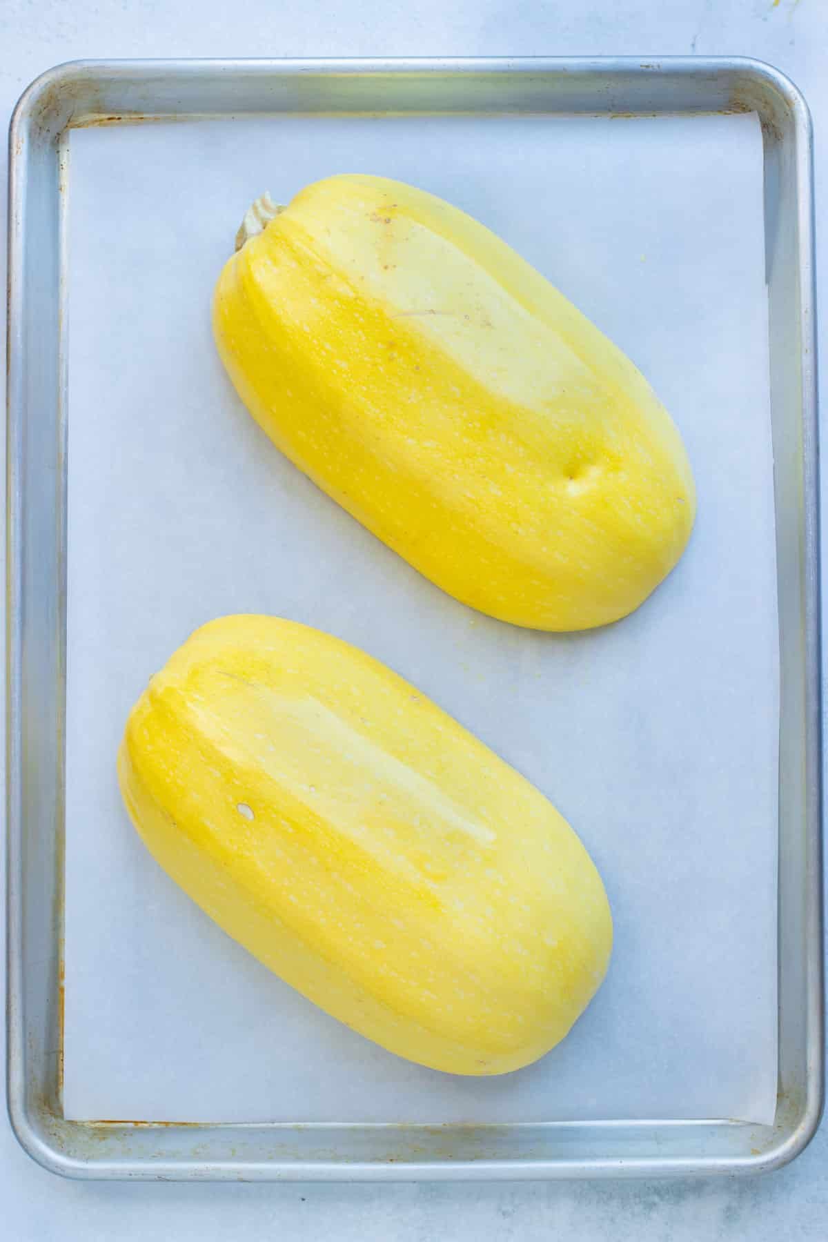 Lay spaghetti squash face down on parchment paper on a large baking sheet before being roasted.