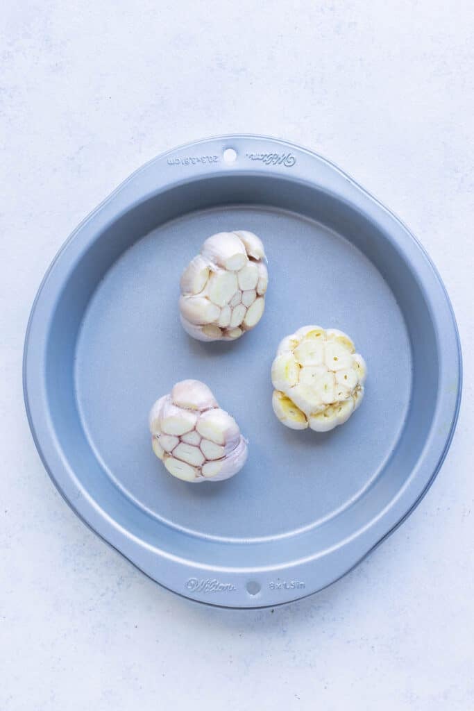 The prepared heads of garlic are placed inside a tin before covering and roasting.