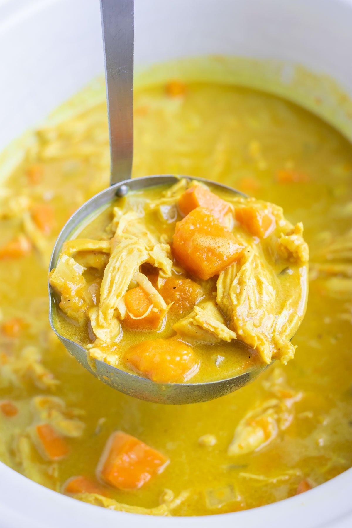A ladle scoops out a flavorful and healthy yellow chicken curry.