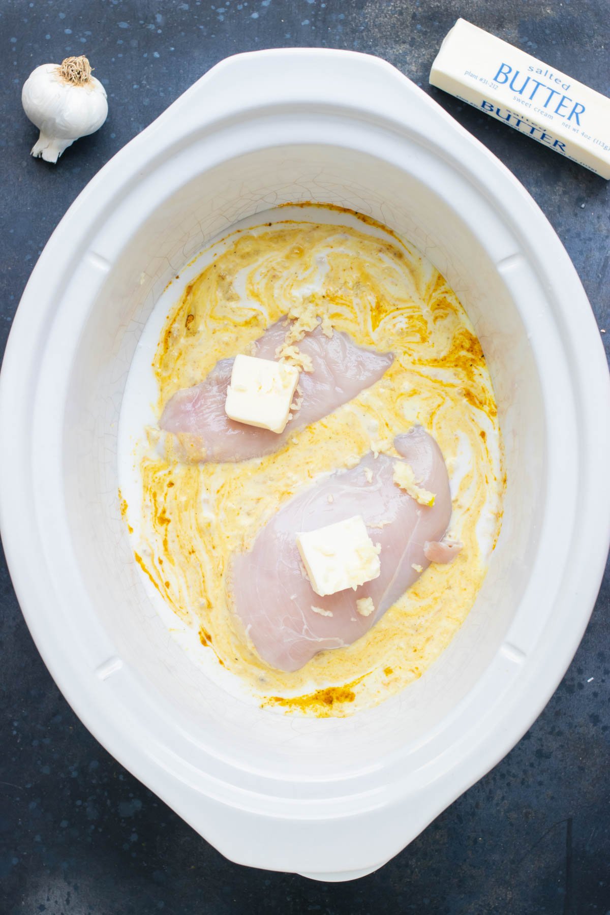 Chicken and butter are added to the slow cooker bowl.
