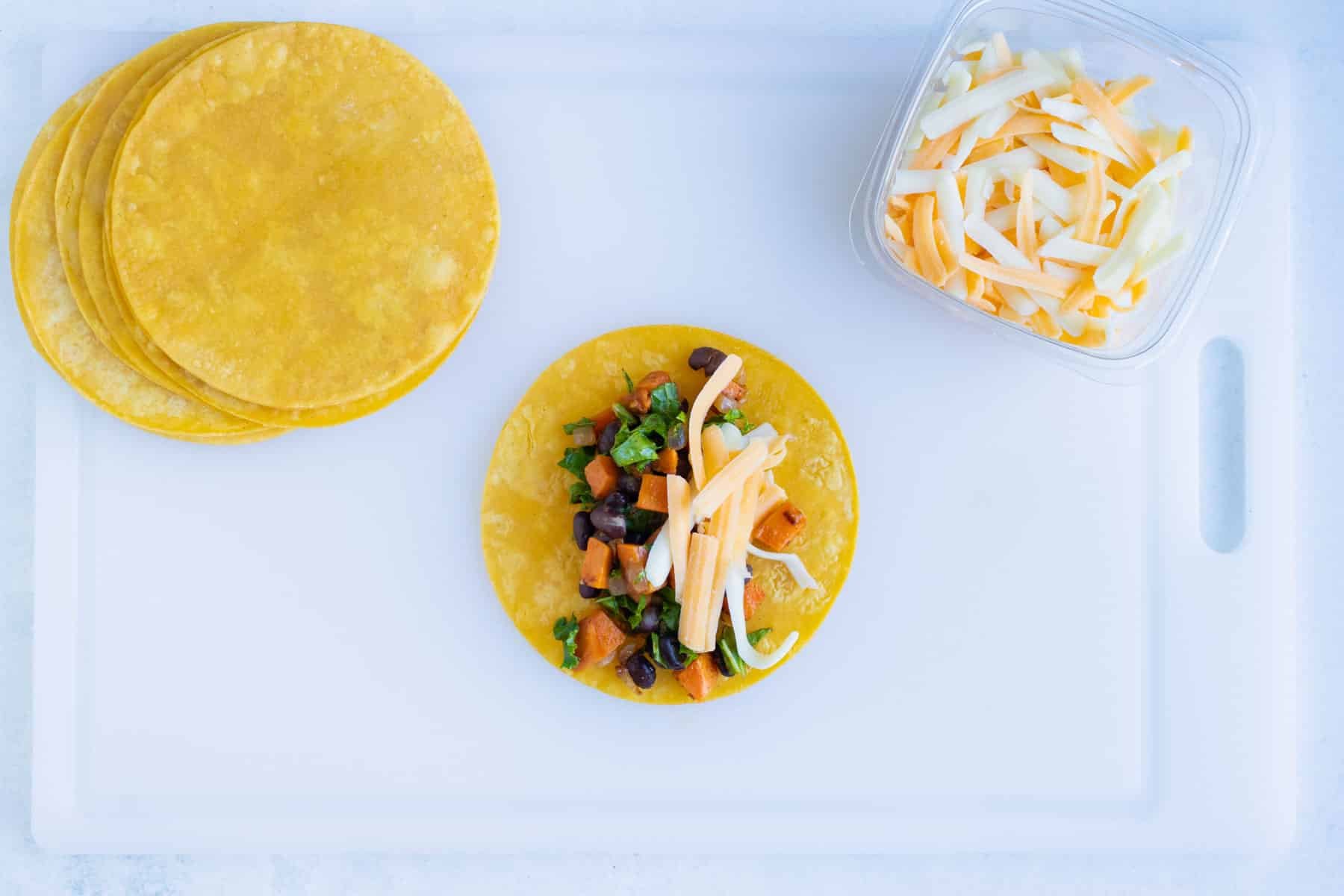 Corn tortillas are filled with the sweet potato black bean filling and shredded cheese.