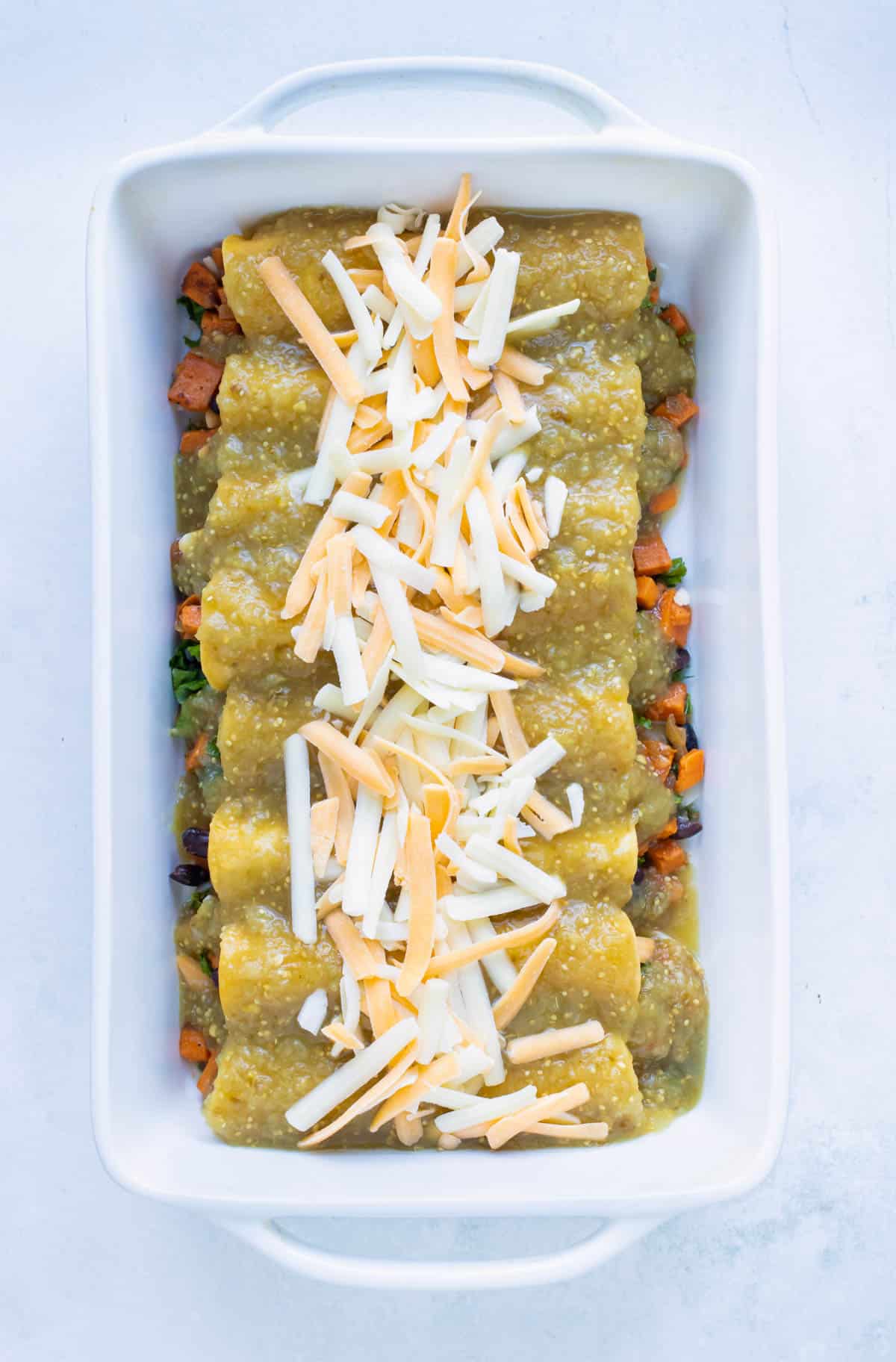 Enchiladas are covered with salsa and cheese is added before baking.