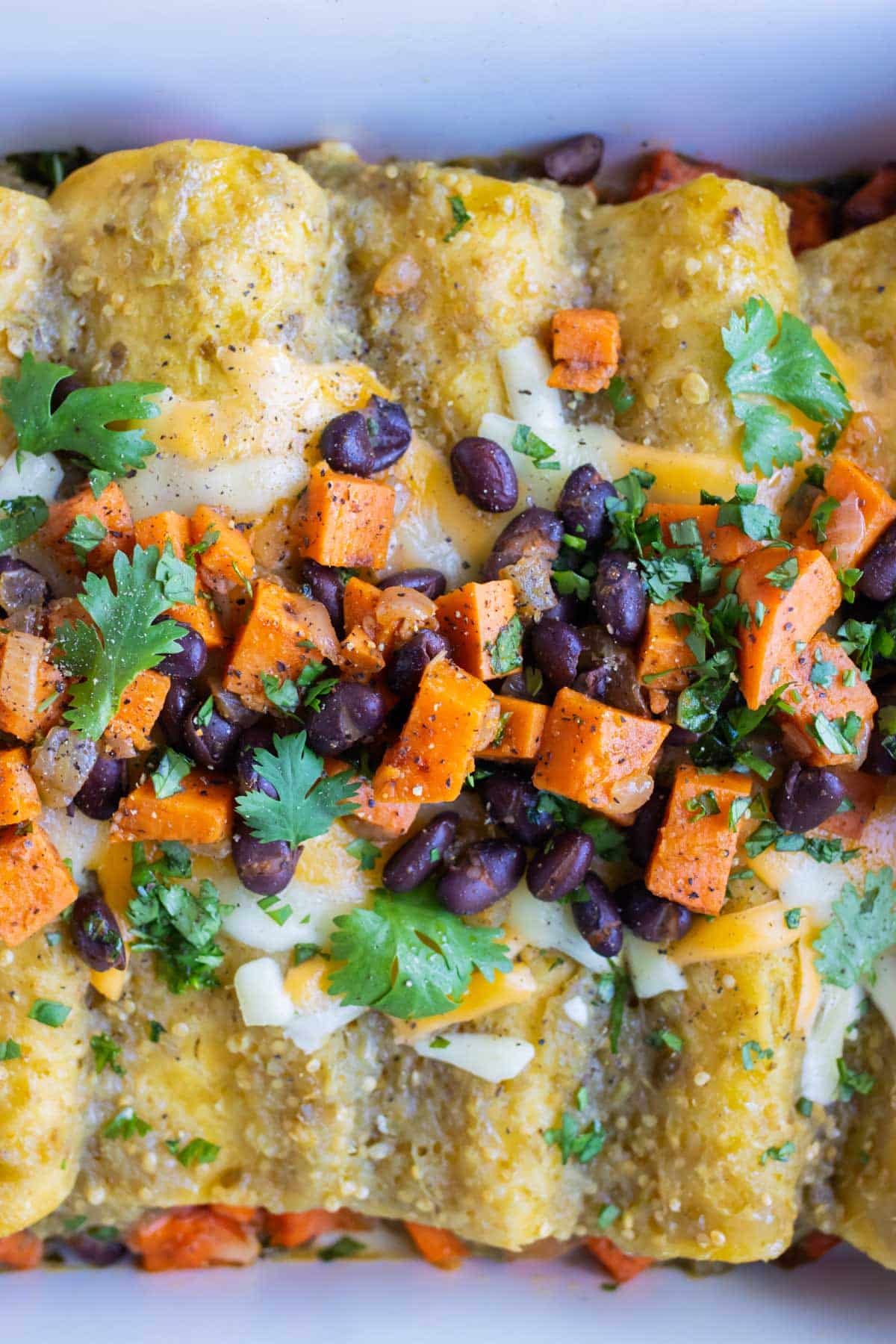 Close up photo of baked enchiladas topped with extra filling and fresh cilantro.