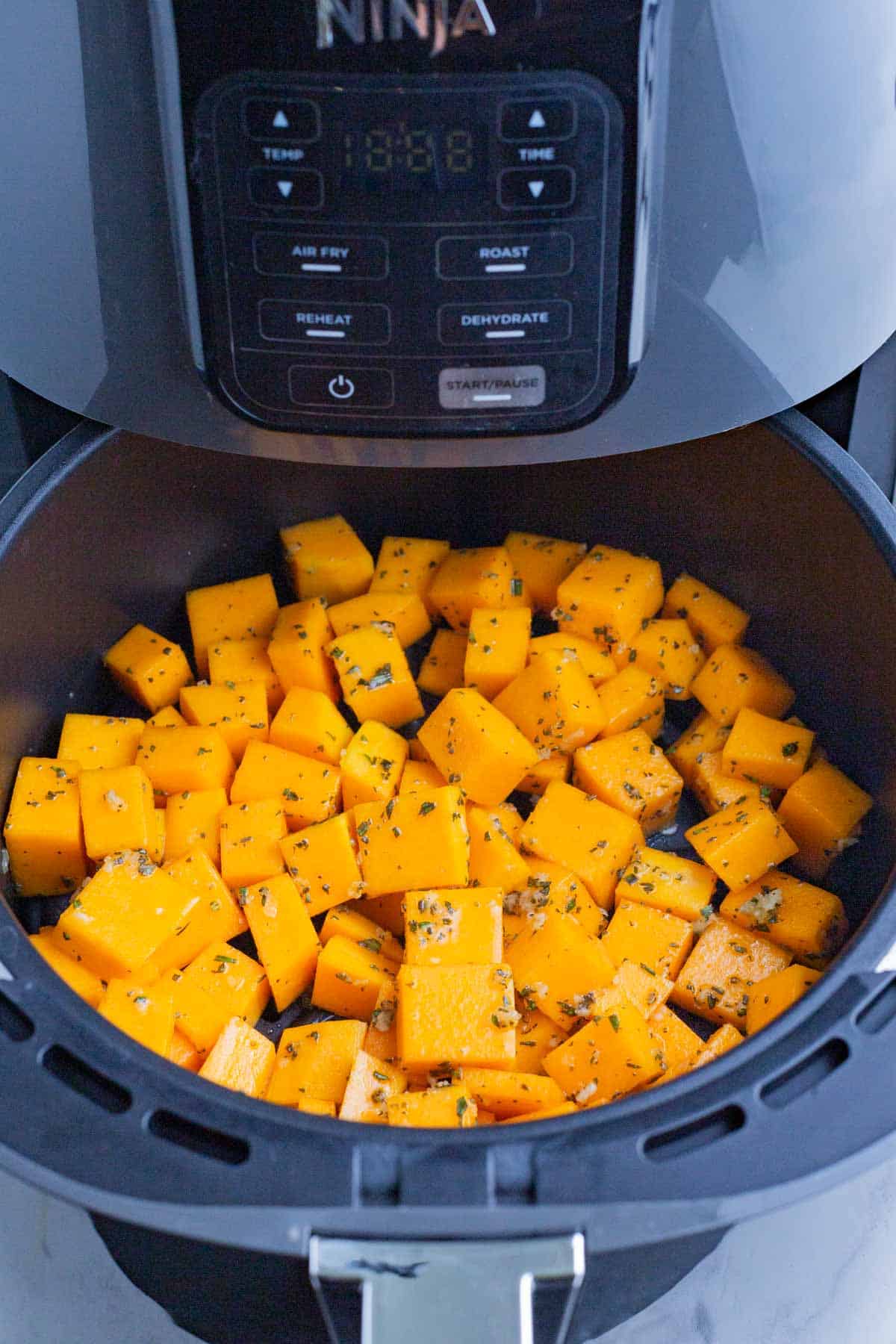 Seasoned butternut squash cubes are cooked in an air fryer.