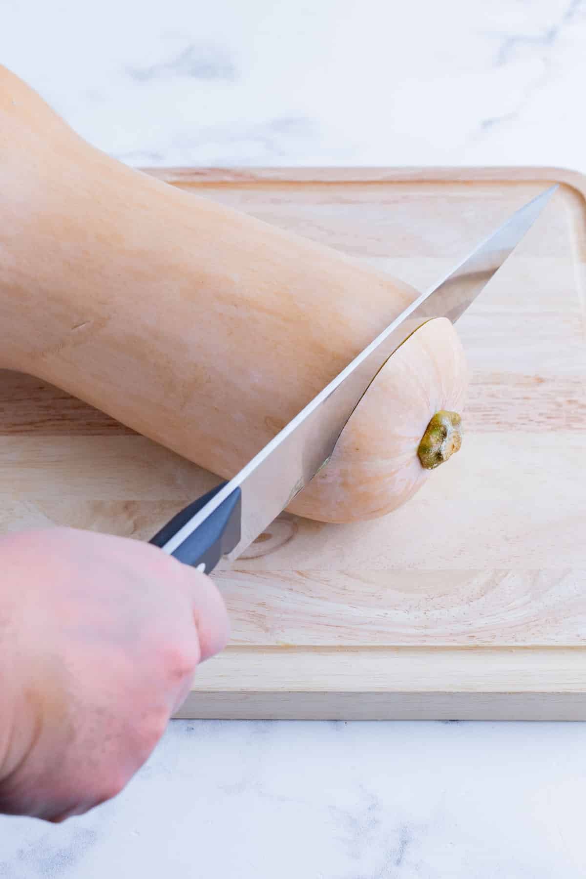 A knife trims the end of a butternut squash off.