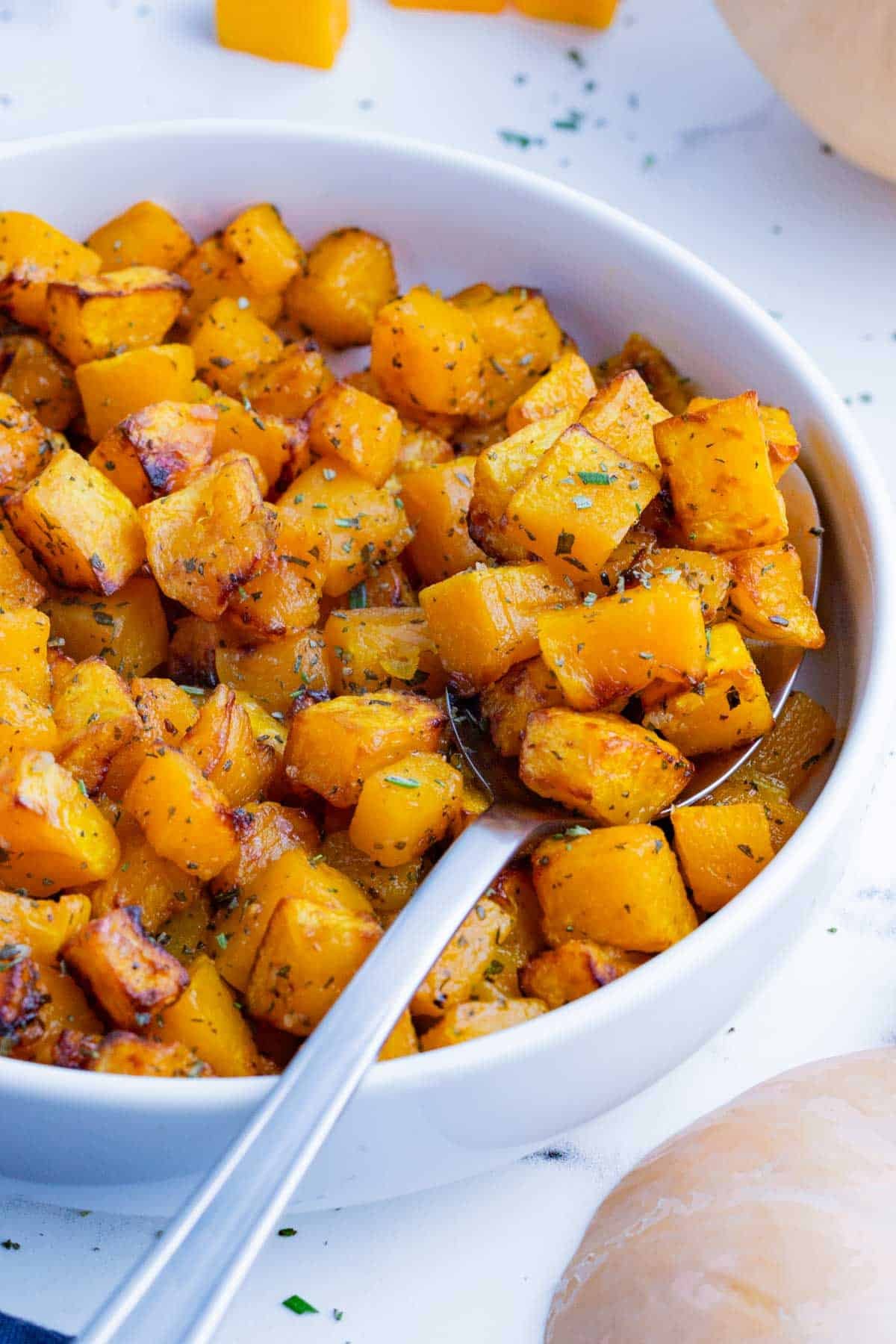 A spoon scoops butternut squash cooked in an air fryer out of a bowl.