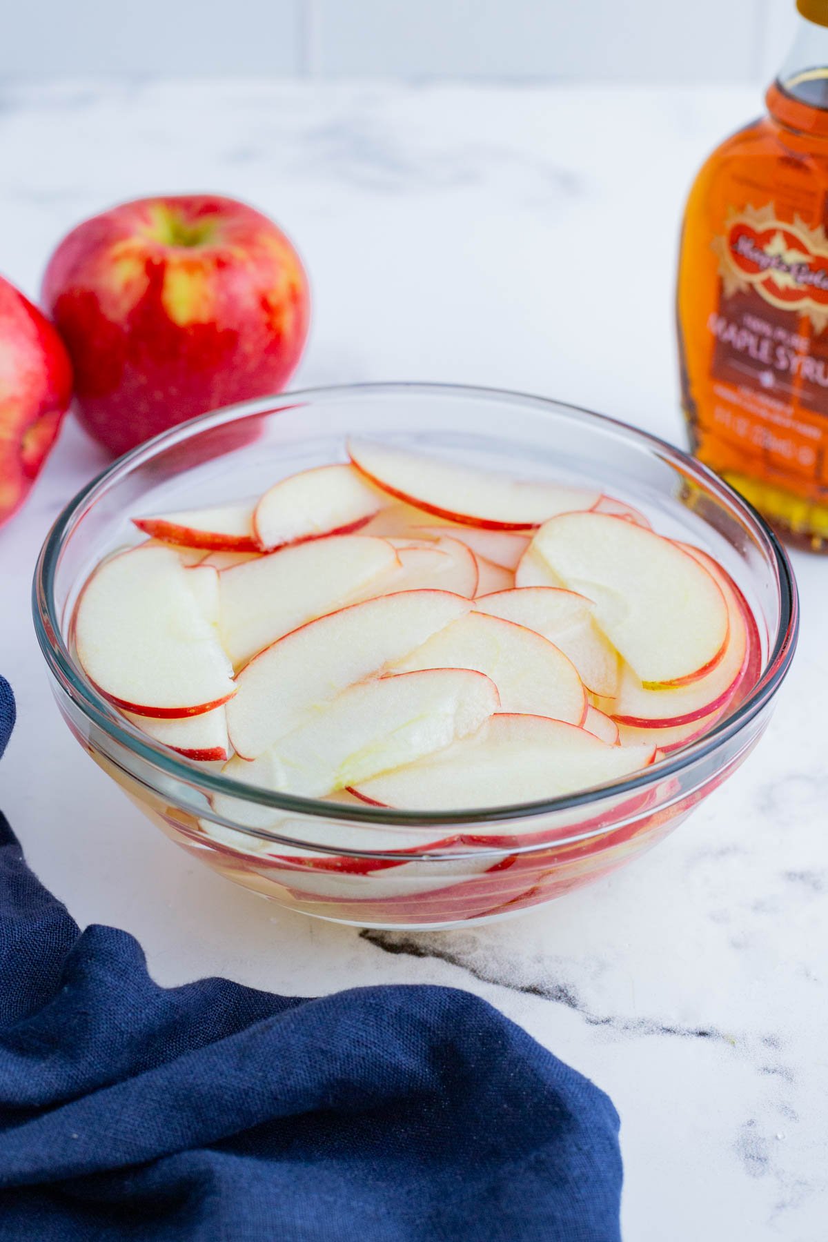 Thinly sliced apples being soaked in honey water in a glass bowl.